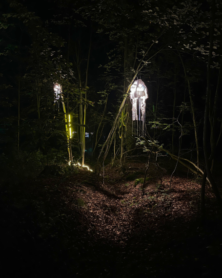 Zwei leuchtende Figuren stehen in einem dunklen Wald zwischen Bambusstämmen.