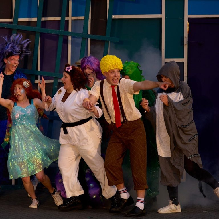 Bunte Kostüme, fröhliche Darsteller auf der Bühne, Aufführung mit dynamischer Atmosphäre.