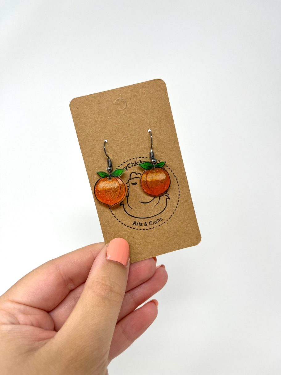 Eine Hand hält eine Karte mit Pfirsich-Ohrringen daran.