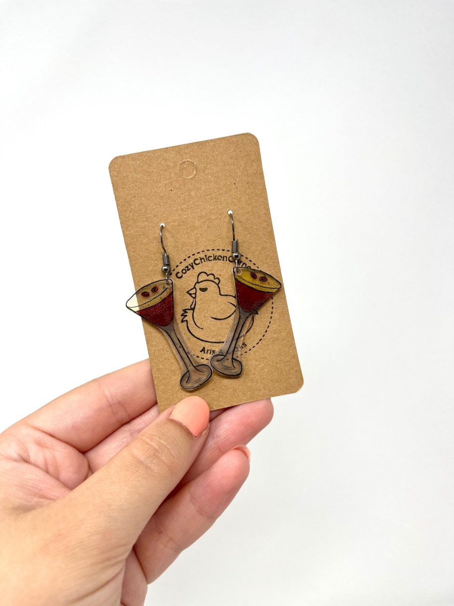 Eine Hand hält eine Karte mit Espresso Martini-Ohrringen daran.