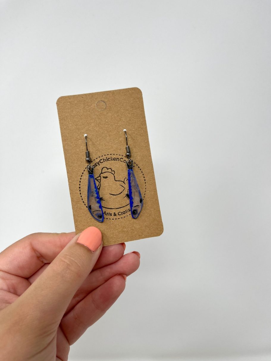 Eine Hand hält eine Karte mit Fisch-Ohrringen daran.